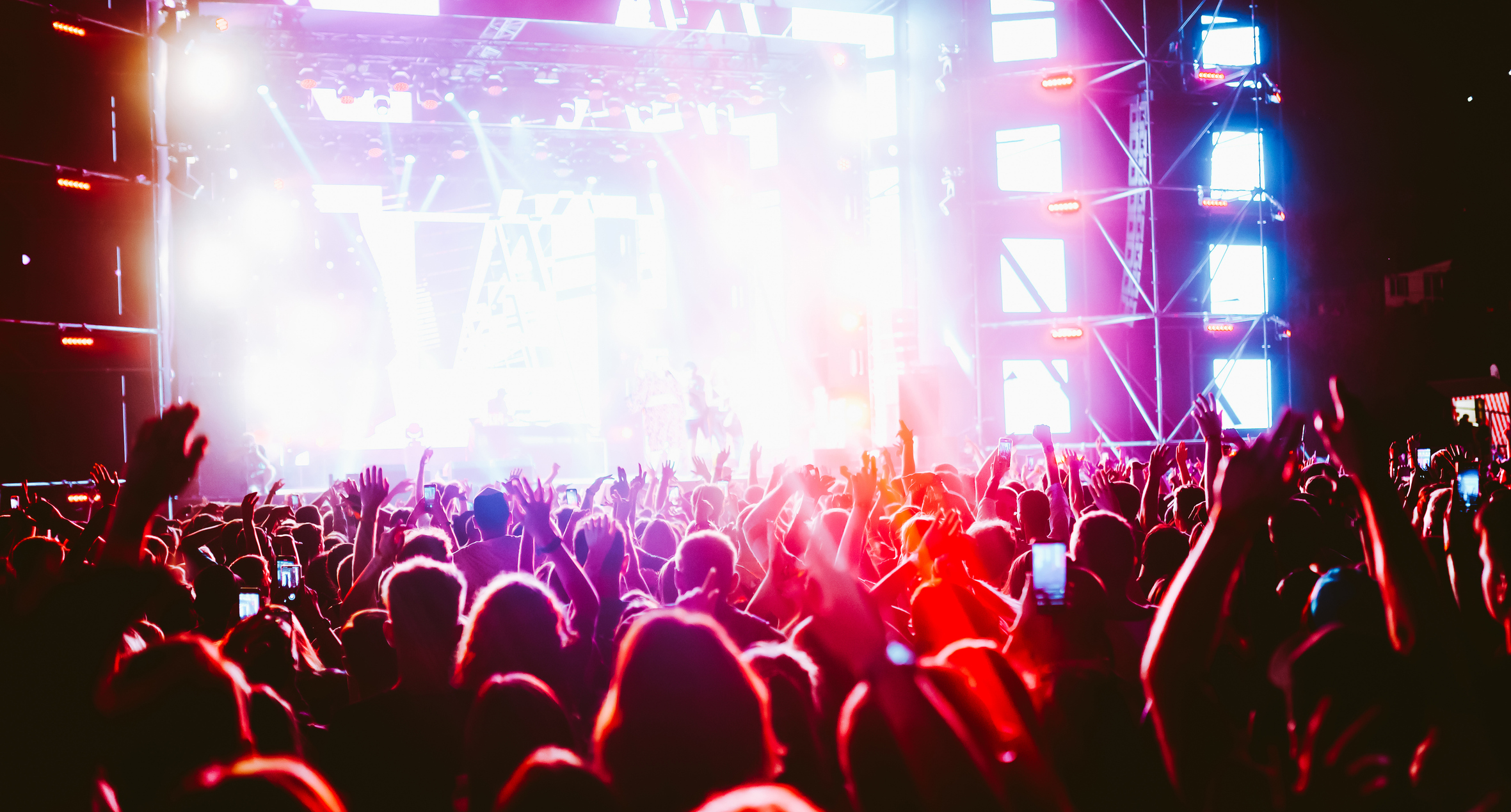 Crowd at concert. Stage lights and hands in the air.